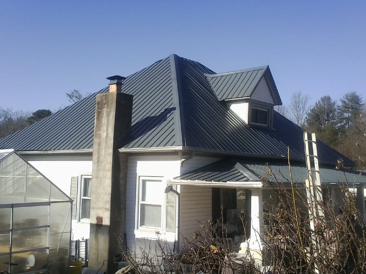 Dark blue standing seam metal roof on a white farmhouse with dormer — Slate & Tile Roof Repair by Roofing Brothers in Belt