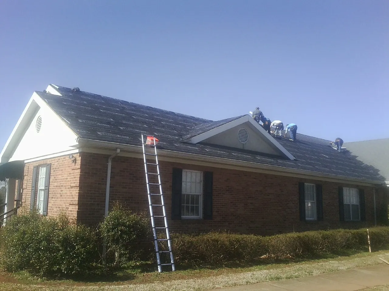 Crew tearing shingles off a brick ranch roof with a ladder set — Emergency Roof Repair work by our crew in Belt