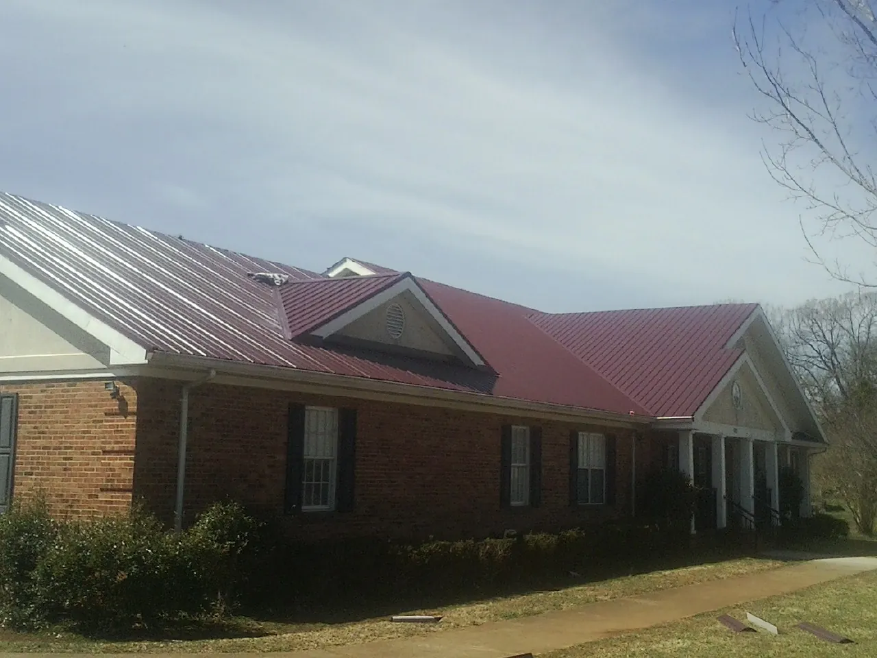 Red metal roof with gabled entries on a long brick building, from a Hail Damage Roof Repair job in Belt
