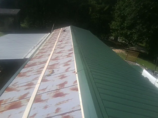 Old rusted panels beside newly installed green metal roofing — Wind Damage Roof Repair by Roofing Brothers in Belt