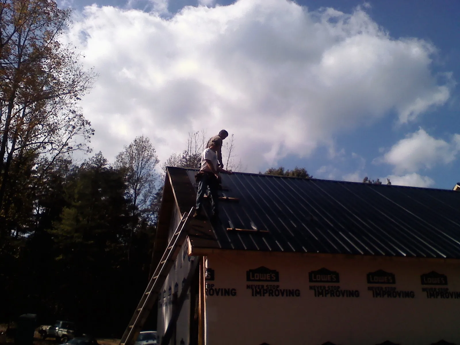 Roofer fastening dark metal panels high against a cloudy sky, from a Roof Inspection job in Belt