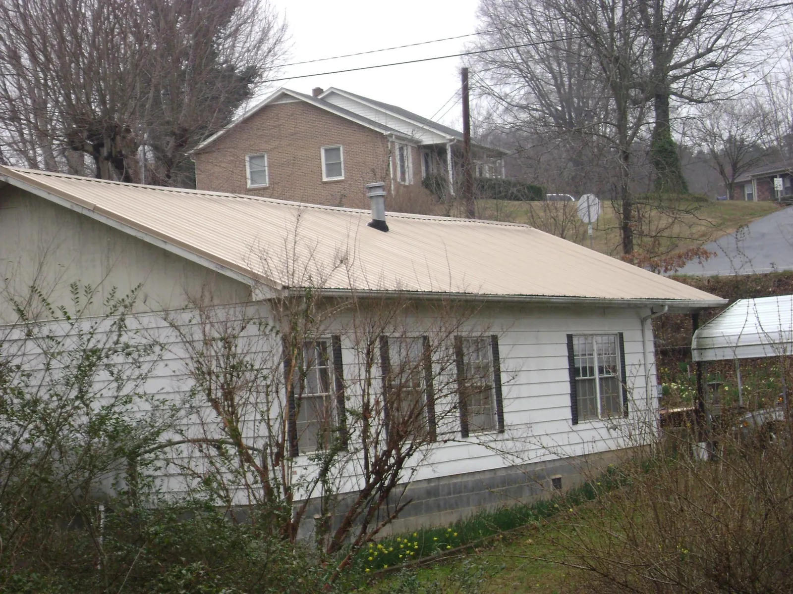 Tan metal roof on a white sided house set into a hillside — Commercial Roofing by Roofing Brothers in Belt