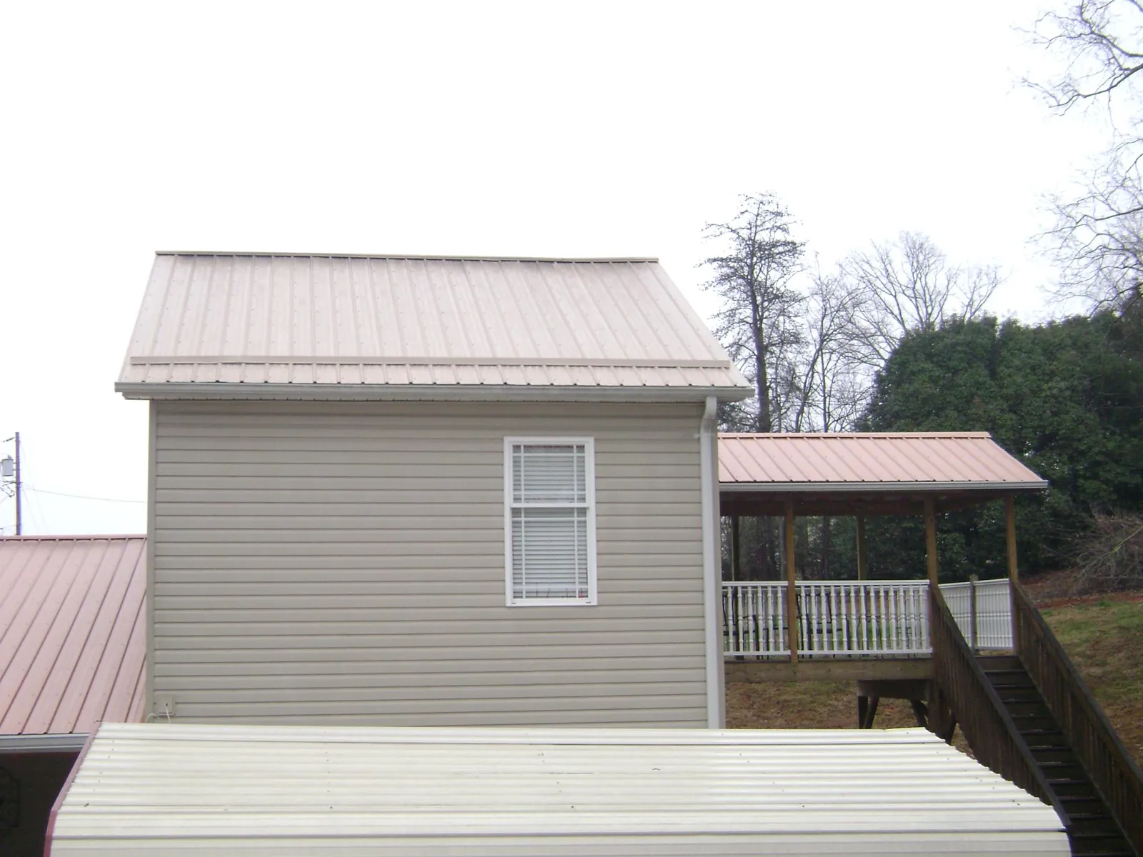 Tan metal roofs on a two story addition and attached porch, from a Roof Replacement job in Belt