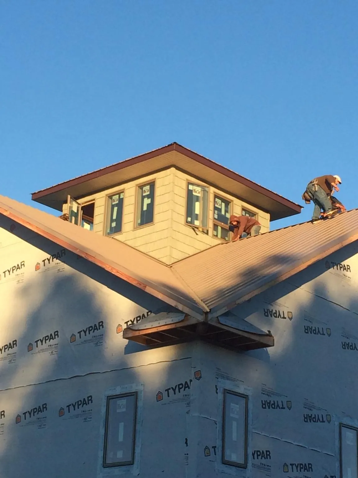 Roofers working around a rooftop cupola on a new metal roof at sunset — Roof Waterproofing in Belt by Roofing Brothers